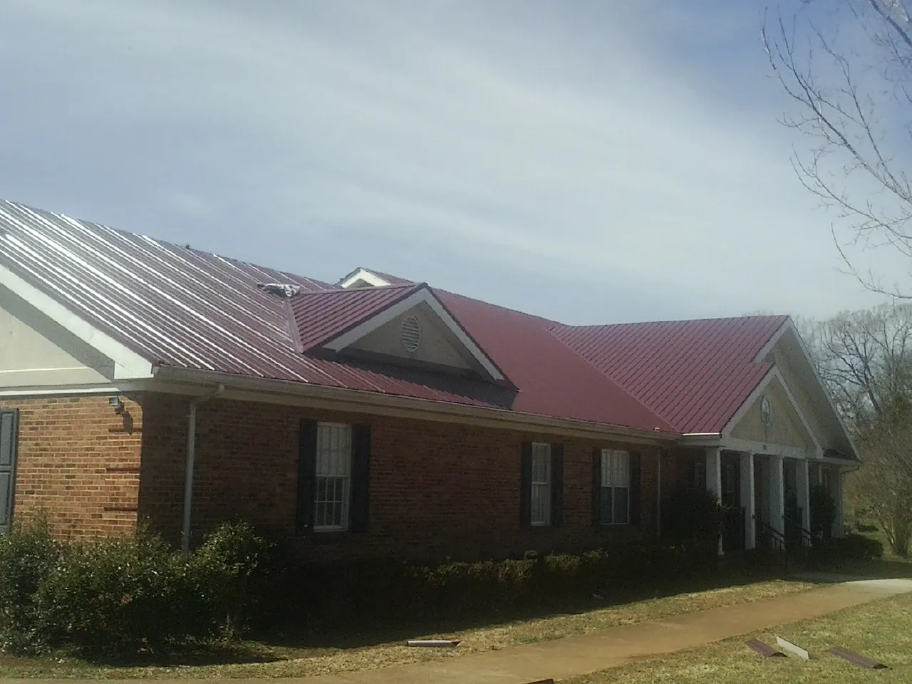 Red metal roof with gabled entries on a long brick building, from a Hail Damage Roof Repair job in Evergreen Park