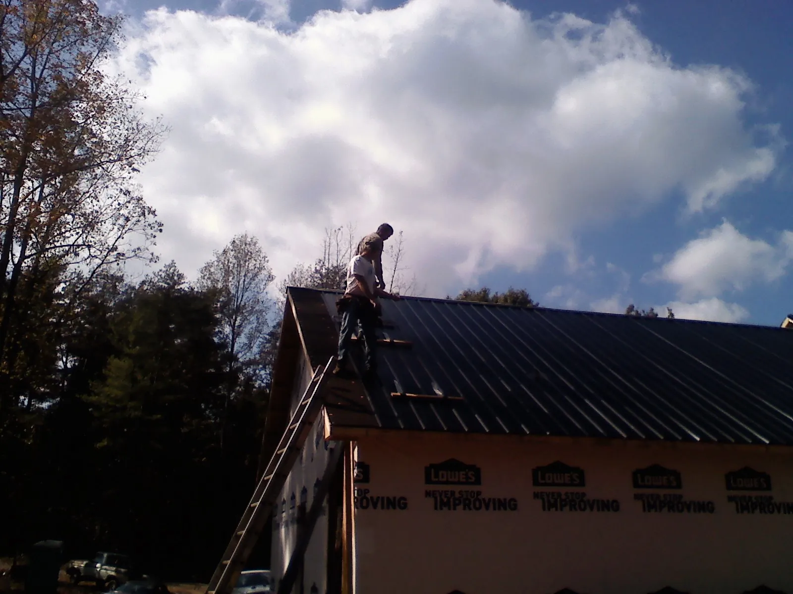 Roofer fastening dark metal panels high against a cloudy sky, from a Roof Inspection job in Evergreen Park