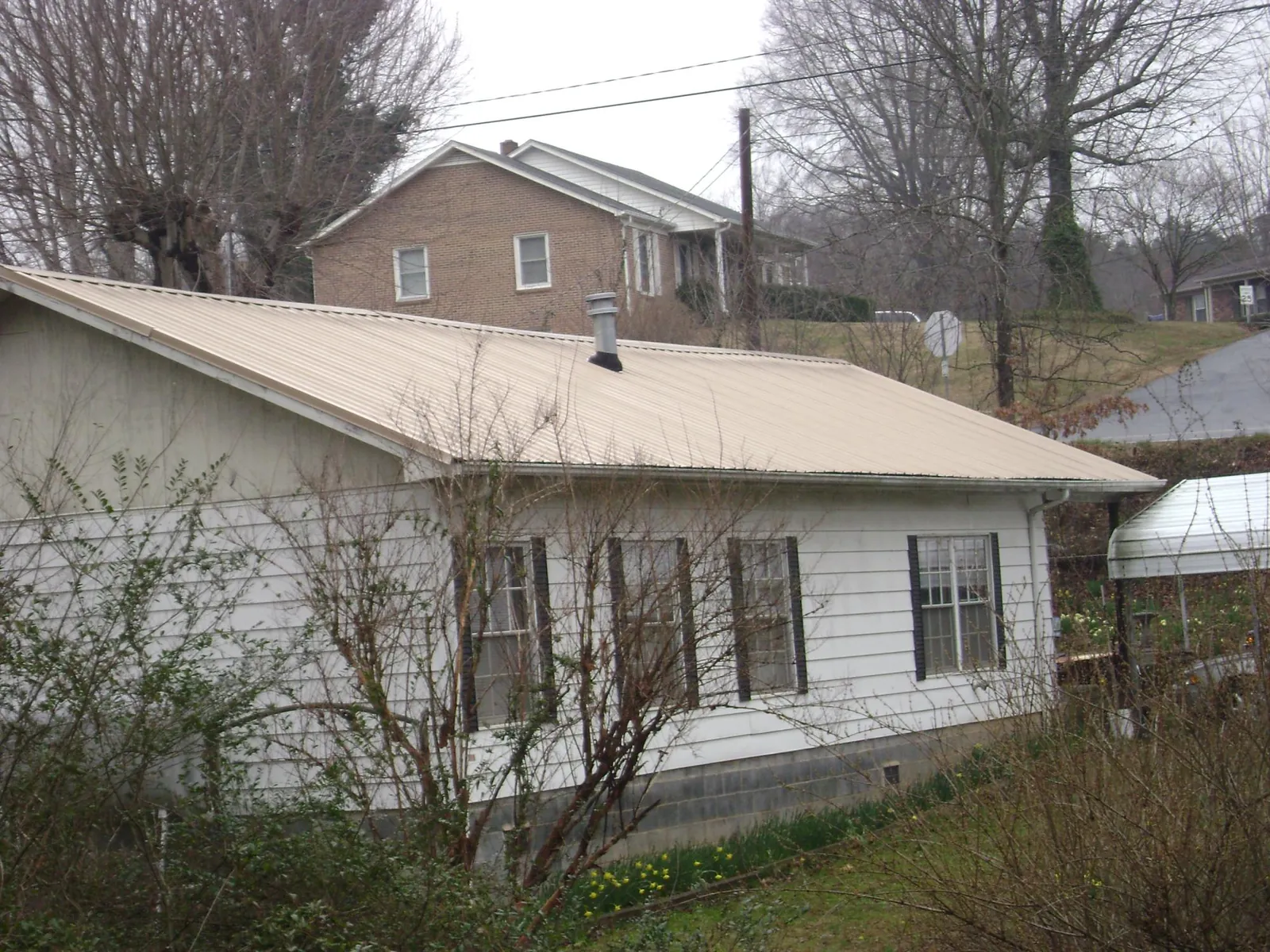 Tan metal roof on a white sided house set into a hillside — Commercial Roofing by Roofing Brothers in Evergreen Park